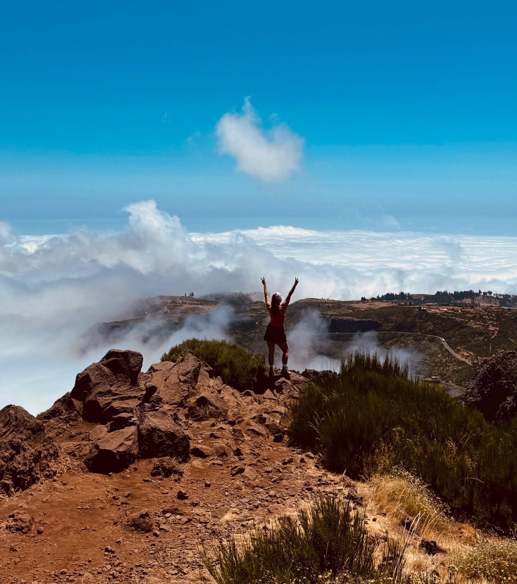 Fenja steht mit erhobenen Armen auf einem Felsen über den Wolken